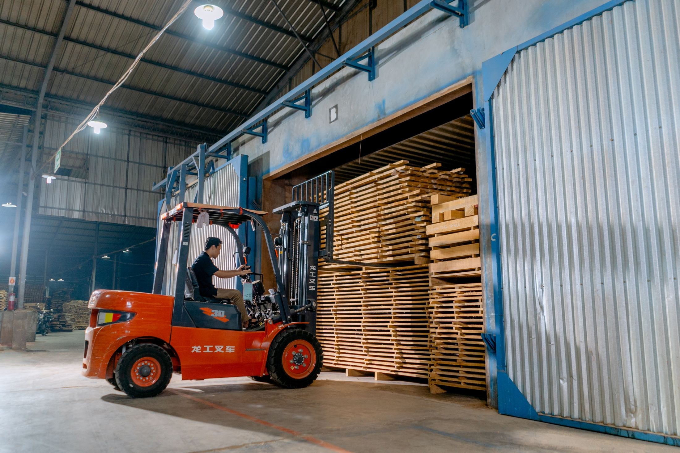 Forklift operator handling stacked lumber inside a warehouse