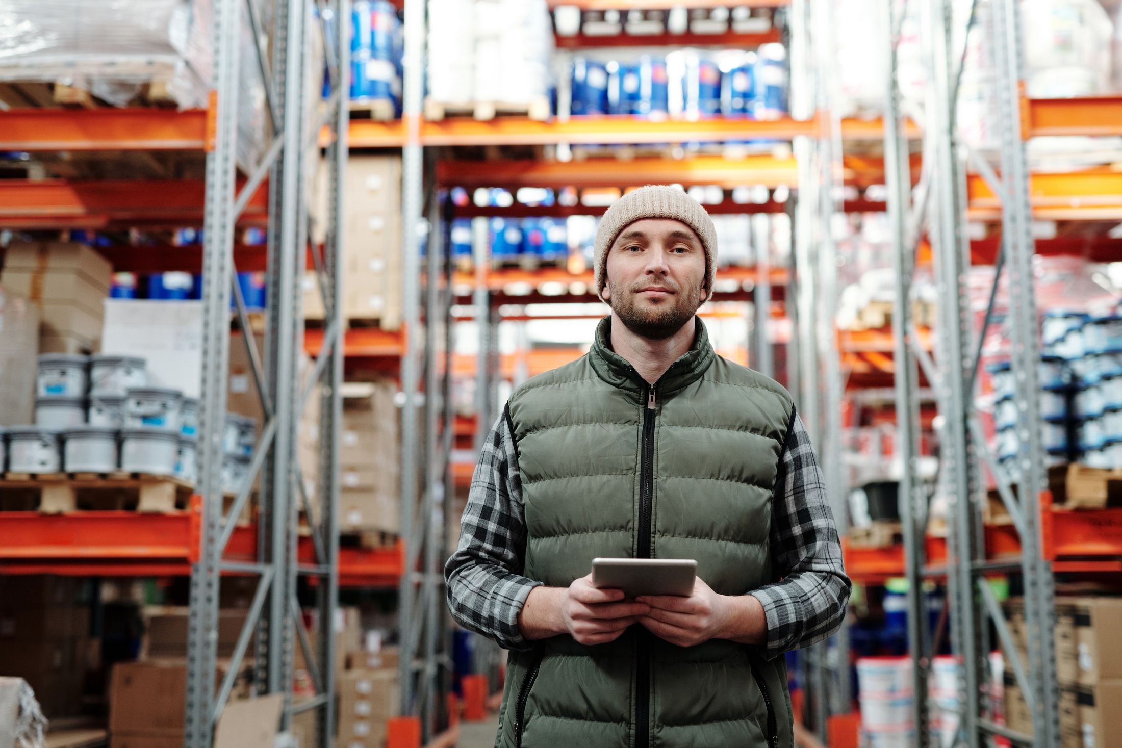 Warehouse worker checking a tablet beside stocked shelves